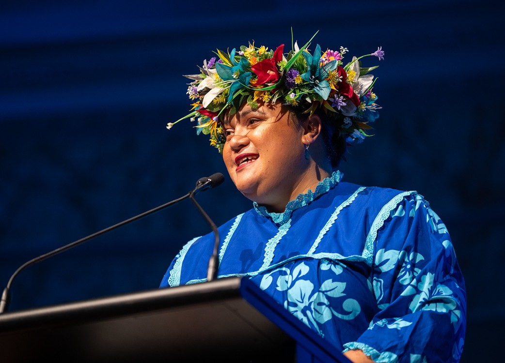 A woman in traditional Pacific Islander dress speaking at a podium